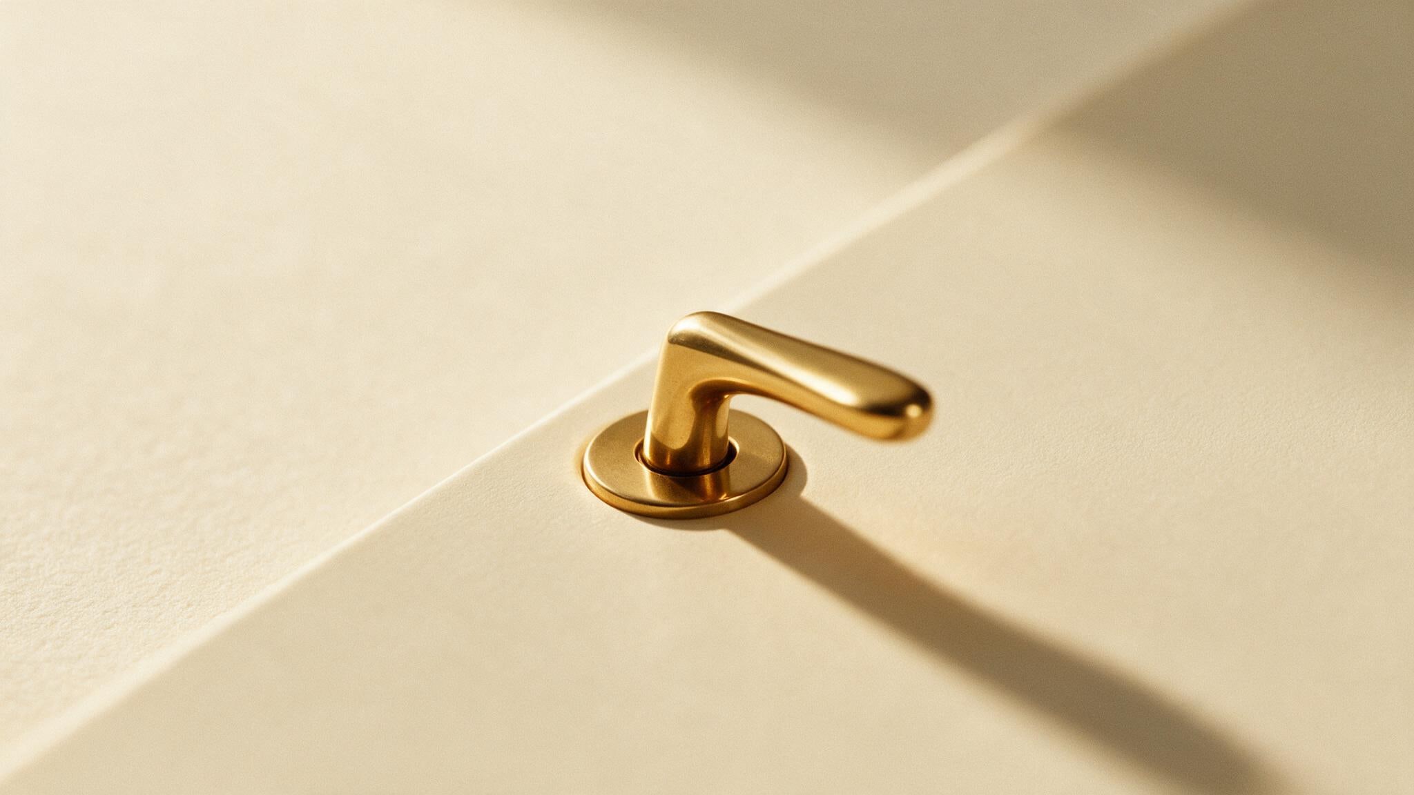 A brass door handle mounted on a smooth cream panel with no visible door around it, lit from one side.